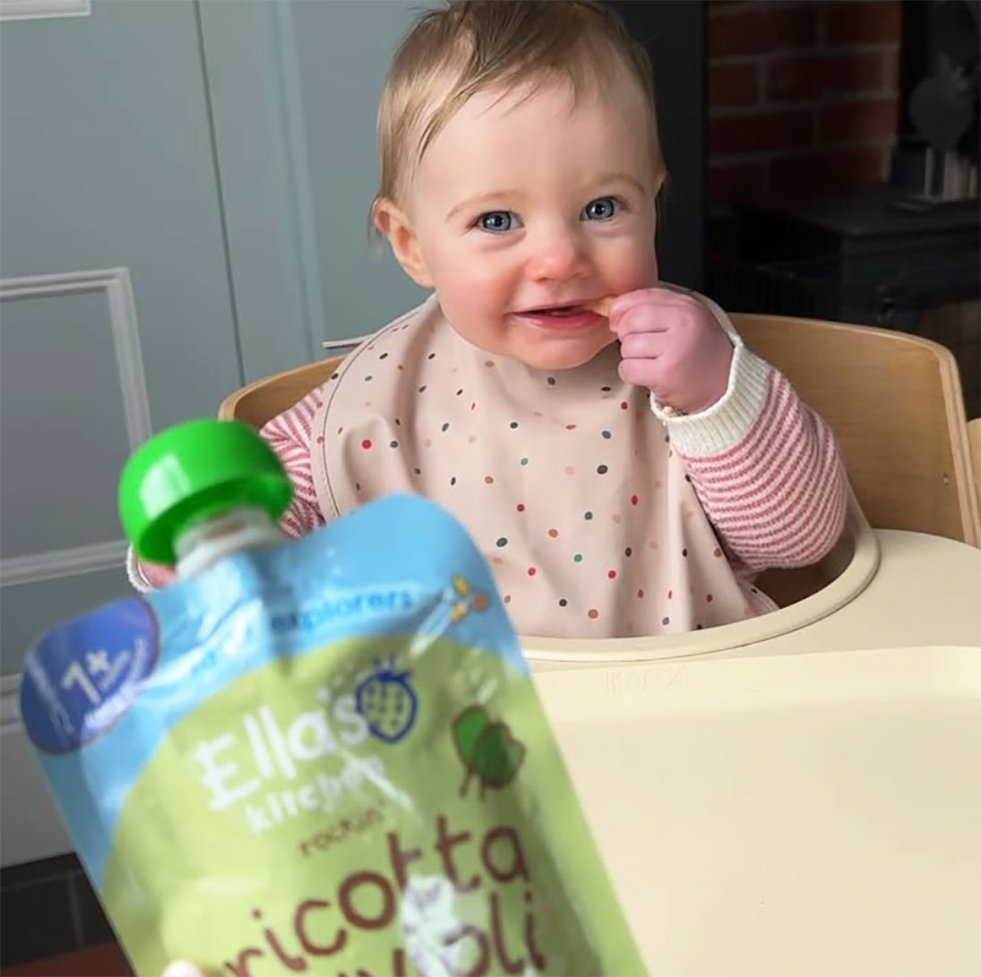 http://A%20happy%20toddler%20being%20fed%20an%20Ellas%20Kitchen%20brand%20baby%20food%20pouch.
